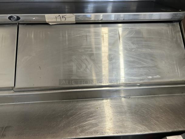 Stainless steel kitchen appliance with two sliding doors, showing moderate wear. Tag with "115" handwritten. Perfect for commercial use.