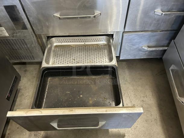 Stainless steel kitchen appliance drawer open displaying perforated and solid trays, moderate wear visible.