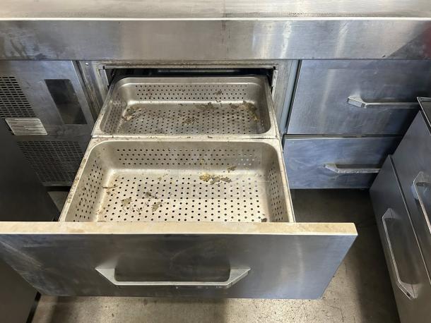 Stainless steel commercial kitchen drawer unit with dual perforated pans, showing signs of use. Ideal for food storage or prep.