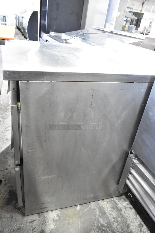 Stainless steel undercounter cooler with 2 drawers, 115 volts, 1 phase. Visible wear and scratches on surface. Ideal for commercial use.