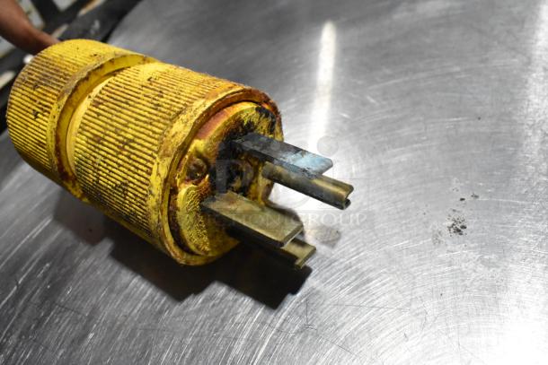 Yellow industrial plug with three-prong connectors on a metal surface, showing signs of rust and wear.