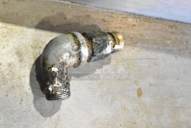 Rusty elbow pipe fitting on a metal surface, covered in grime and corrosion.