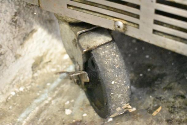 Close-up of a commercial caster on a Beverage Air SPE48-18M stainless steel prep table. Caster shows signs of wear.