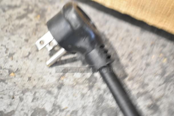 Blurry close-up of a black power plug from a 2021 True TSCI-600R-G-PH commercial cooler merchandiser.