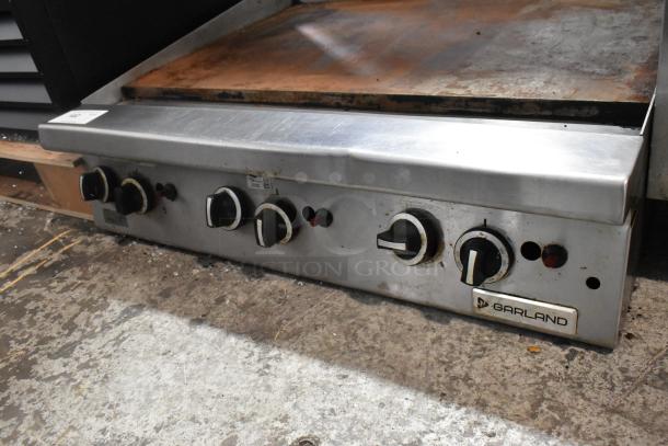 Garland stainless steel commercial gas flat top griddle, featuring multiple control knobs, showing signs of use.