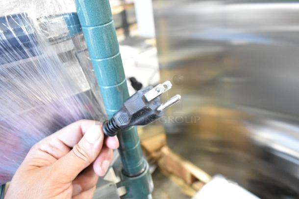 Avantco 177LT87 food dehydrator plug, held in hand, attached to plastic-wrapped unit, indicating 120V power requirement.