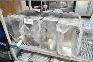 55 new stainless steel drop-in bins, lightly scratched, in protective plastic on metal rack. Auction lot tag visible.