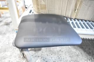 Box of brand new black seat cushions with minor blemishes, showing one cushion on a cart. Durable material, ideal for seating.
