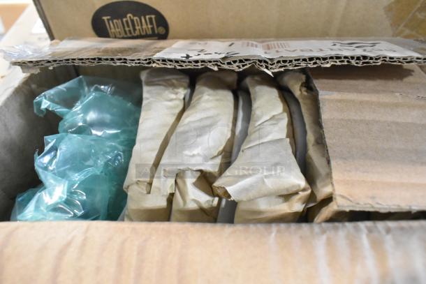 Cardboard box containing wrapped items, including a Tablecraft Acacia Round Display Board and other scratch and dent items.