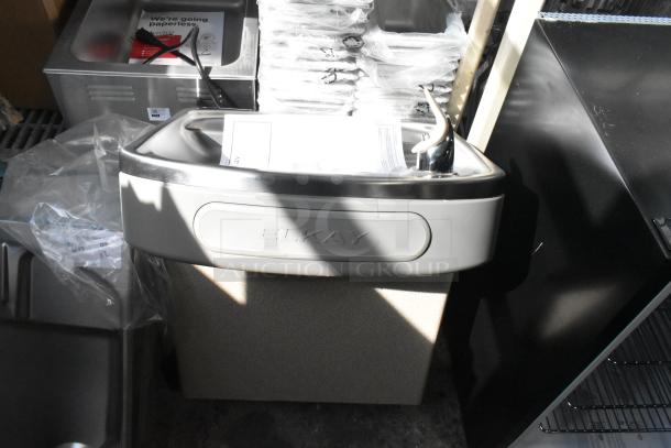 Brand new Elkay wall mount water fountain, silver finish. Minor scratch and dent. Model tag visible on unit.