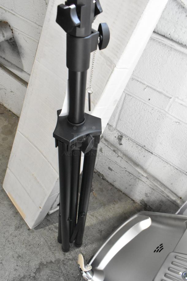 Brand new scratch and dent metal tripod stand, black, with adjustable height, minor cosmetic flaws visible.