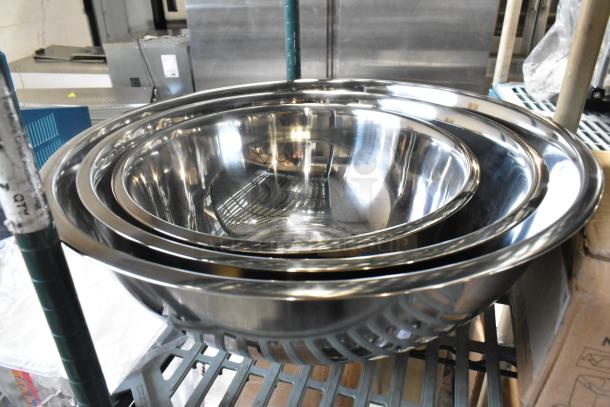 Three new metal bowls with slight scratches and dents, stacked on a shelf. Shiny stainless steel construction, durable design.
