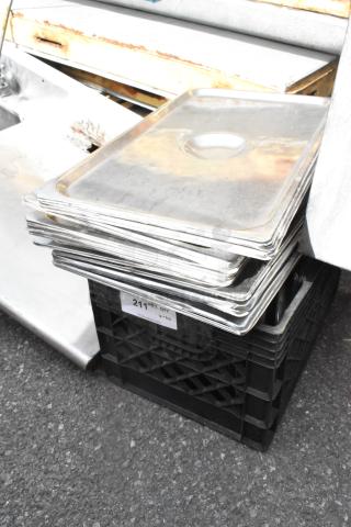Stack of metal full-size drop-in bin lids, showing surface wear, atop a black crate labeled "211 in qty v-lot."