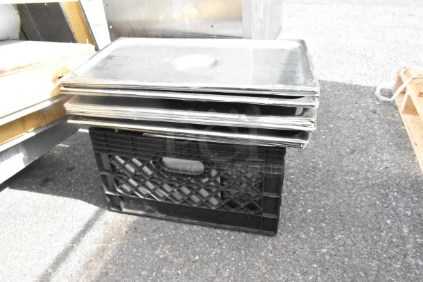 Stack of metal full-size drop-in bin lids on a black crate, moderate wear, ideal for storage or kitchen use.