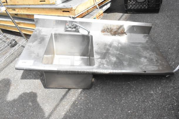 Stainless steel counter with sink bay, faucet, and handles. No legs. Some surface wear and rust visible. Item tagged "212."
