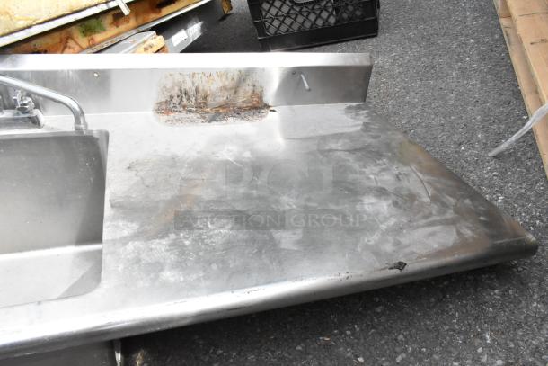 Stainless steel counter with sink bay, faucet, and handles. No legs. Visible wear and rust on surface.