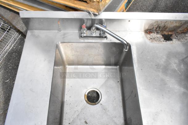 Stainless steel counter with sink bay and faucet, visible wear, no legs.