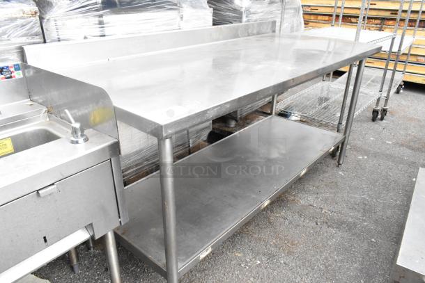 Stainless steel table with backsplash and under shelf, used condition, durable design, ideal for commercial kitchens.