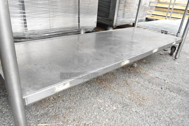 Stainless Steel Table with under shelf, showing signs of use, suitable for industrial or kitchen settings.