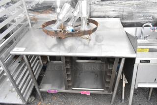 Stainless steel table with under shelf, pan rack, and additional contents. Used condition with visible wear.