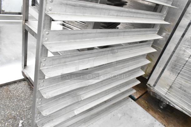 Metal pan transport rack with multiple shelves, mounted on commercial casters for easy mobility. Visible signs of use.