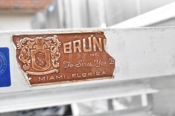 Metal pan transport rack on commercial casters, featuring a Brunelli Inc. label from Miami, Florida, indicating food service use.