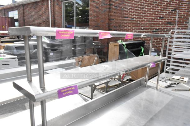 Stainless steel table with under shelf and 2-tier over shelf, featuring catering labels, in used condition.