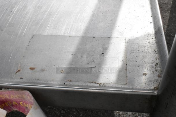 Stainless steel table surface, showing signs of wear. The table includes an under shelf and two-tier over shelf for added storage.