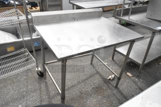 John Boos stainless steel table with a high backsplash, sturdy legs, and slightly worn surface. Ideal for commercial kitchens.