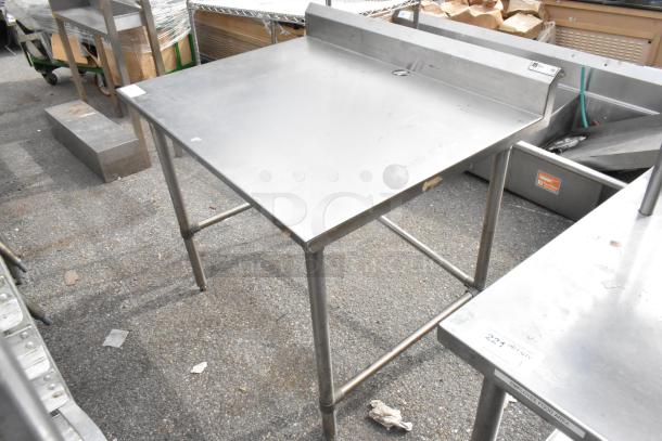John Boos stainless steel table, sturdy design, some surface wear, with backsplash and cross-braced legs. Suitable for kitchen use.