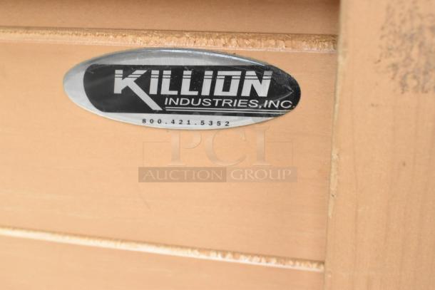 Killion Industries metal label on wooden surface, featuring company logo and contact number.