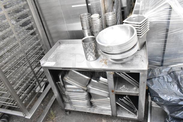 Stainless steel table with stacked drop-in bins and bowls; used condition with some wear. Item tag visible on table edge.