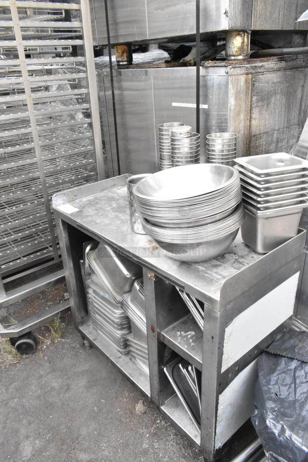 Stainless steel table with drop-in bins, metal bowls, visible wear; ideal for kitchen or catering use.