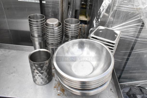 Stainless steel table with various kitchen items, including drop-in bins and metal bowls. Slight surface wear visible.