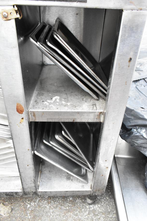 Stainless steel table with drop-in bins and metal bowls, visible wear, rust spots, and sturdy shelving for kitchen use.