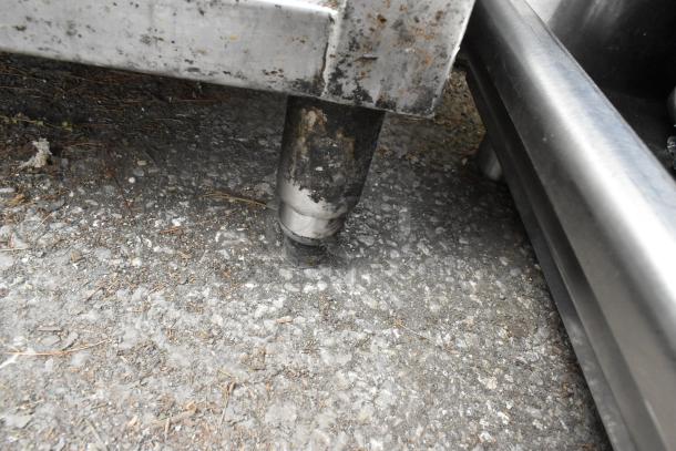 Stainless steel table leg with visible wear, part of a table including drop-in bins and metal bowls.
