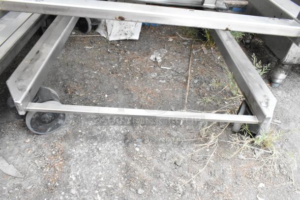 Metal commercial pan transport rack with wire shelves on sturdy commercial casters, shown in outdoor setting.
