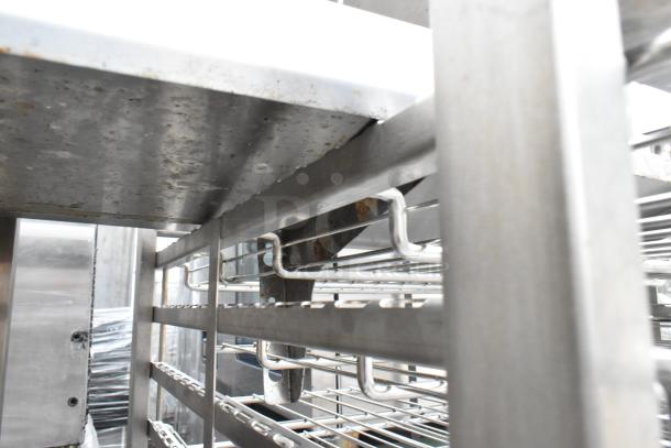 Metal commercial pan transport rack with wire shelves, commercial casters, and visible wear. Ideal for kitchen use.