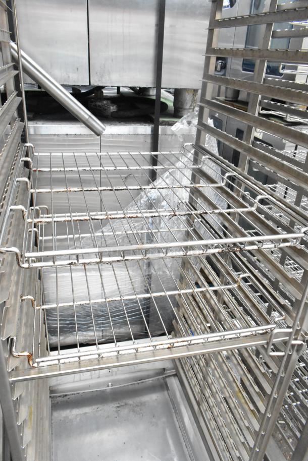 Metal commercial pan transport rack with wire shelves on commercial casters, shows slight rust on edges, sturdy condition.