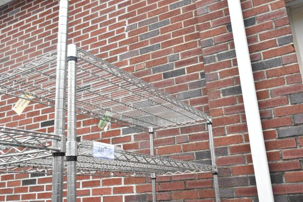 Chrome finish 5-tier wire shelving unit on commercial casters, shown against a brick wall with tags indicating dismantling requirements.