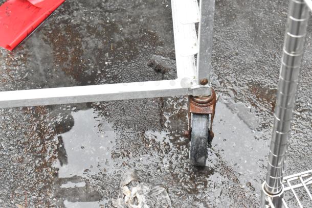 Metal commercial pan transport rack with rusted commercial caster on wet ground.