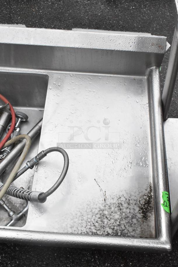 Stainless steel 3 bay sink with dual drain boards, no legs. Includes plumbing attachments, some wear visible.