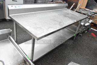 Stainless steel table with under shelf and backsplash in good condition, features brushed metal finish and visible surface moisture.