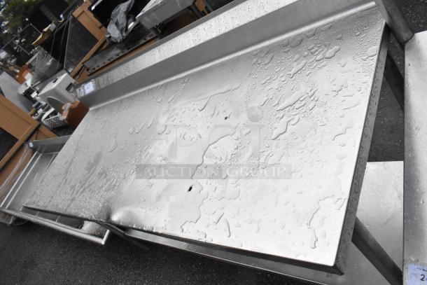 Stainless steel table with under shelf and backsplash, water droplets visible, sturdy condition. Ideal for kitchen use.