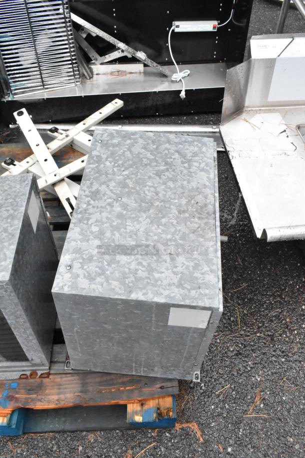 Two metal commercial condensers with metal pieces on a wooden pallet. Galvanized finish, some wear indicated.