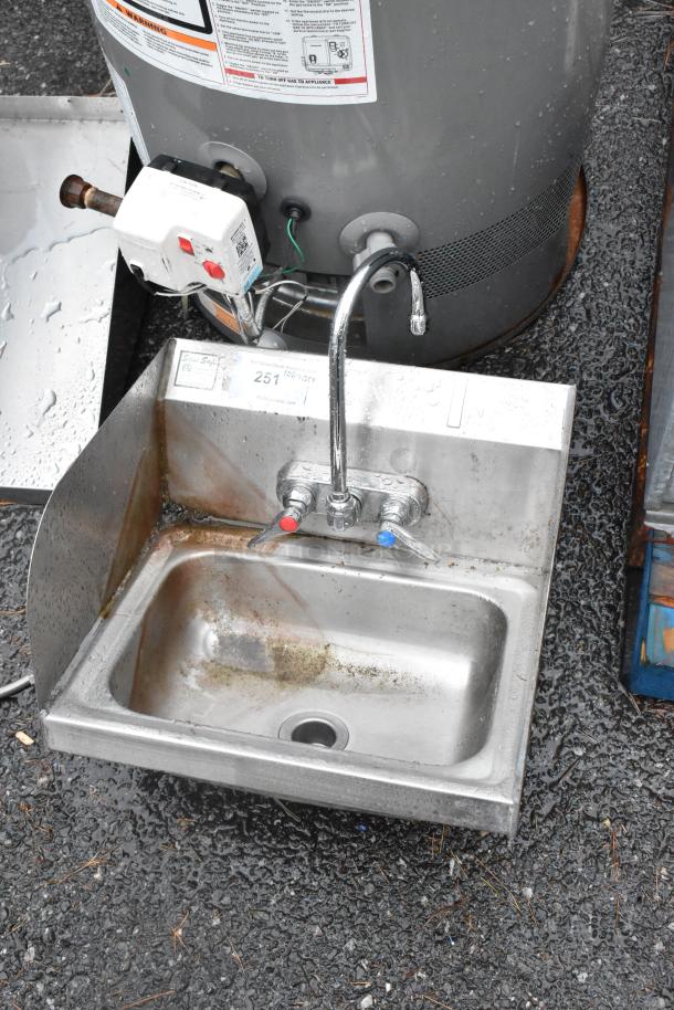 Stainless steel wall mount sink with faucet, dual handles, and side splash guards. Used condition, visible label.