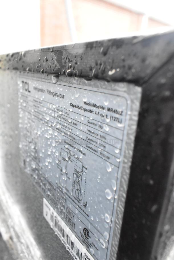 Close-up of TCL MR45ZZ cooler label showing model details, 4.5 cu ft capacity, 120V, 1-phase. Water droplets on surface.