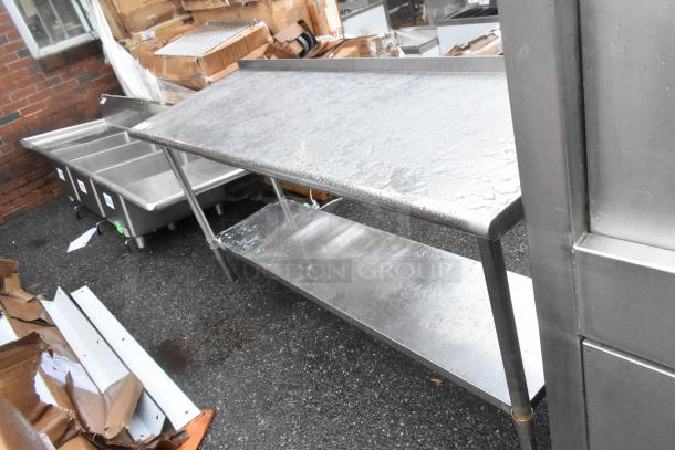 Stainless steel table with under shelf, outdoor setting, wet surface, durable design, visible signs of use.
