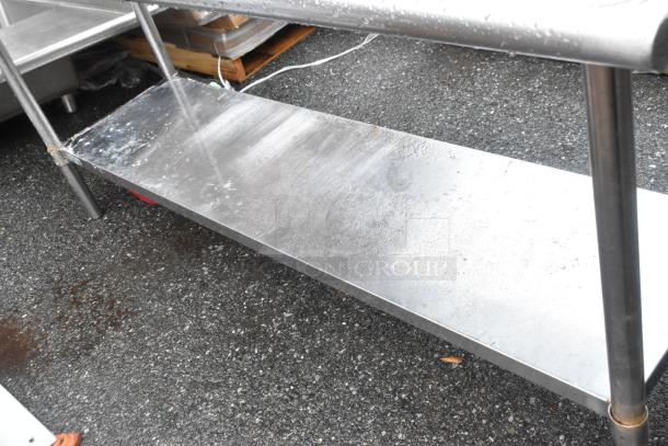 Stainless steel table with under shelf, showing slight wear. Ideal for kitchen or industrial use, durable construction.