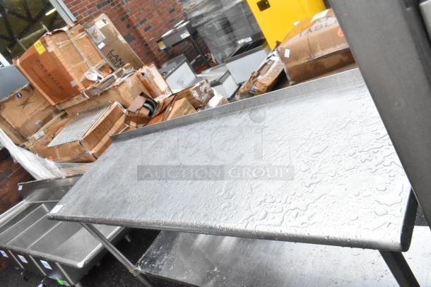 Stainless steel table with under shelf, showing water droplets on surface, in used condition. Ideal for storage or kitchen use.